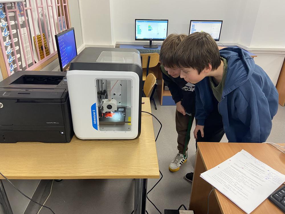 Dwóch chłopców przygląda się pracującej drukarce 3D drukującej gwiazdkę.