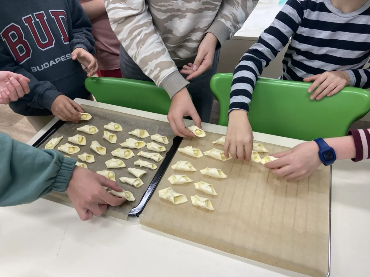 Przygotowanie do pieczenia. Uczniowie układają ciastka na blaszanej podstawie przykrytej papierem do pieczenia.